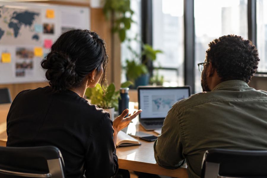 Two colleagues reviewing a world map on a laptop during a strategy conversation